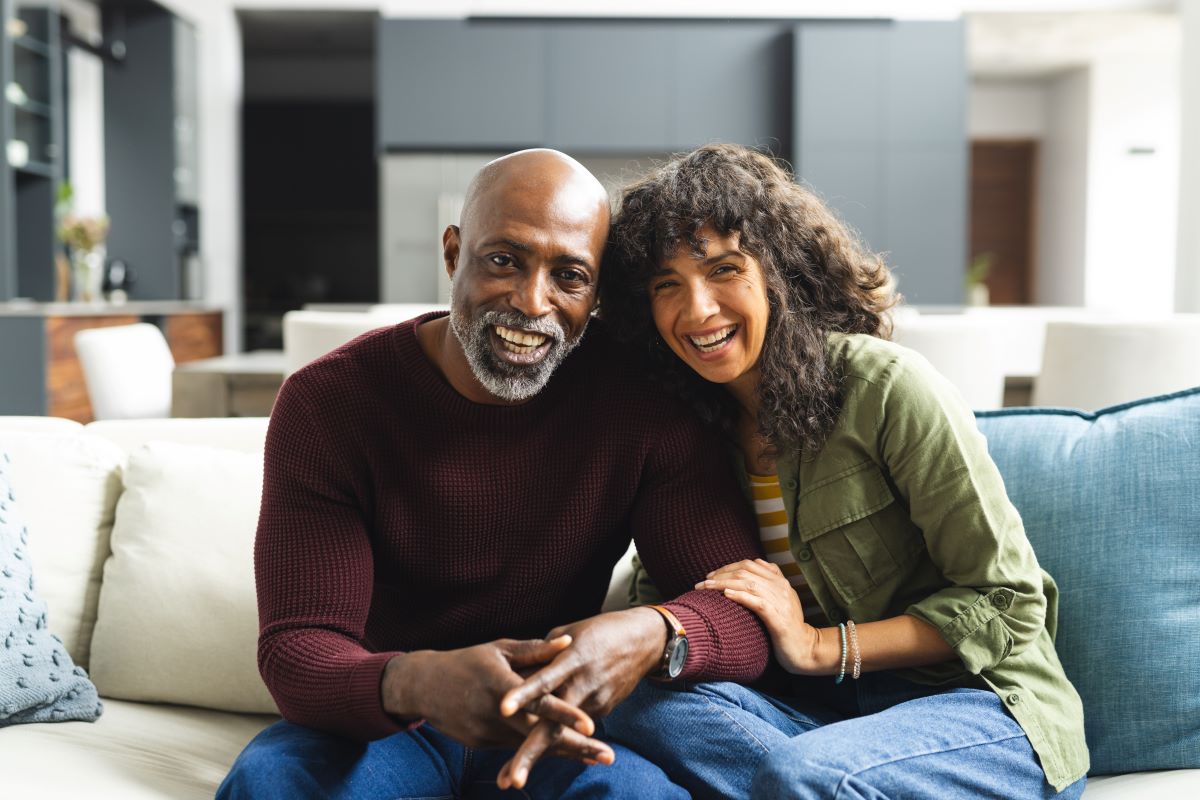 Happy mature diverse couple smiling while sitting on a couch